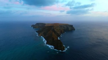 Uçsuz bucaksız sularla çevrili çıplak kayalık bir ada. Arkaplanda gri bulutlar ufku kaplıyor. Madeira Adaları, Portekiz. Hava perspektifi.