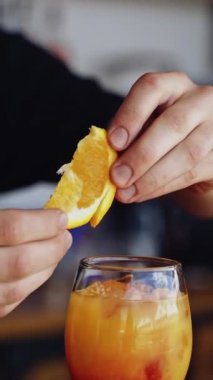 Bar masasında kokteyl hazır. Barmen bardağın üstüne parlak bir içecekle bir dilim portakal koyar. Gece kulübünde bardakla içki. Dikey video