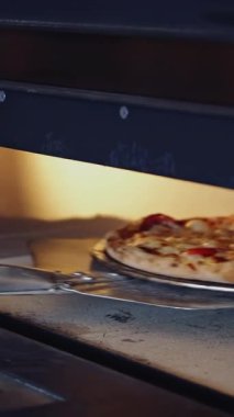 Sıcak, lezzetli pizza. Pizzacı fırından hazır pizzayı çıkardı. Şef, mutfakta spatulayla taze pizza çıkartıyor. Dikey video