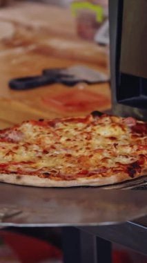 Pizza hazır. Pizzacı pizza yapıyor. Pizza spatulasını kullanarak pizzayı fırından çıkaran şef. Aşçı bitirilmiş pizzayı tabağa koyar. Lezzetli pizza. Dikey video