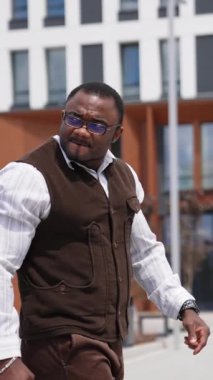 Çok ırklı ve tatmin olmuş genç bir iş adamı başını çevirip dikkatle bir şeye bakıyor. Beyaz tişörtlü şık bir adam iş yerine yürüyor. Başarı, insanlar ve iş konsepti Dikey video