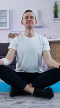 Karantinada yoga yapan sağlıklı bir adam. Spor kıyafetli genç adam evde çalışıyor. Tam uzunluktaki dikey video