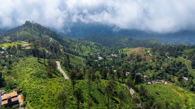 Lush Sri Lanka tepeleri bulutların altında. Sri Lanka 'nın yeşil tepelerinin geniş bir manzarası, dolambaçlı yolları ve bulutlu bir gökyüzünün altındaki dağınık köyleri gösteriyor..