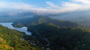Şafak vakti Sri Lanka tepelerinin hava manzarası. Şafakta Sri Lanka 'nın büyüleyici yeşil tepelerini keşfedin, ağaçların arasına kurulmuş sakin bir göl ve dağların üzerinde süzülen sis ile.