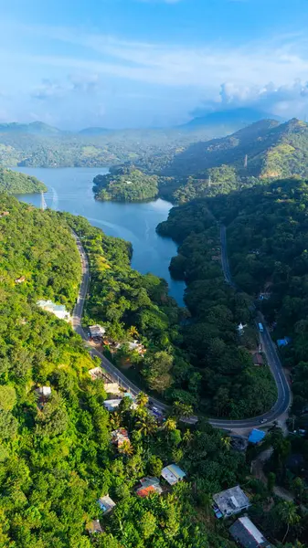 Sri Lanka 'nın yemyeşil manzarasının havadan görünüşü. Sri Lanka 'nın gür tepeleri, adanın çarpıcı doğal güzelliğinin altını çizerek sakin bir su yolu ve dolambaçlı bir yol oluşturuyor..