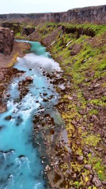 Kayalıklardan akan turkuaz suyu olan nehir. Dik dağlardan çoklu şelaleler düşüyor. İzlanda doğası. Dikey video.