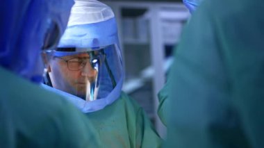 Cerrahlar ameliyat sırasında farları olan koruyucu kasklar takarlar. Doktorlardan biri elinde makas tutuyor. Travma cerrahisinde ekip çalışıyor..