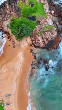 Kumlu sahil kayalık kıyıya çıkıyor. Kayaların üzerinde biraz yeşillik yetişiyor. Üst Manzara. Dikey video.