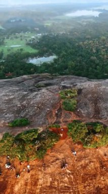 Çırılçıplak bir şekilde kayanın tepesinde yeşillik azaldı. İnsanlar dağın bir tarafında oturup günbatımını seyrediyorlar. Sri Lanka hava görüntüsü. Dikey video.