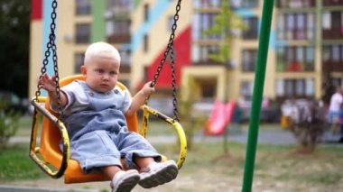 Tatlı oğlan sarı salıncakta oturuyor. Tatlı çocuk arkasını dönüp arkasına bakıyor. Çocuk parkında eğlendik. Bulanık arkaplan.