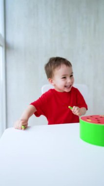 Neşeli çocuk sevimli bir şekilde masasından fırladı. Sevimli oğlan bir oyuncakla oynuyor. Dikey video.