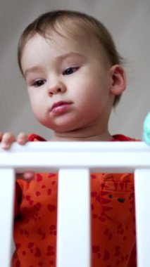 Sevimli tombul yanaklı güzel bebek karyolada duruyor. Elinde emzik tutan sevimli küçük çocuk. Düşük açı. Dikey video