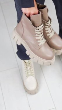 Kadın model, bol pantolon giyiyor ve beyaz traktör tek botlu, elinde bir çift daha bej çizme tutuyor. Yukarıdan bak. Beyaz zemin zemin. Dikey video