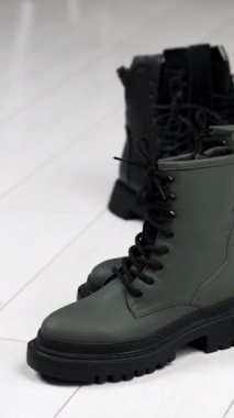 Traktör tabanında iki çift siyah ve gri bot var. Beyaz çizmeli kadın bej ve siyah ayakkabı getiriyor. Dikey video