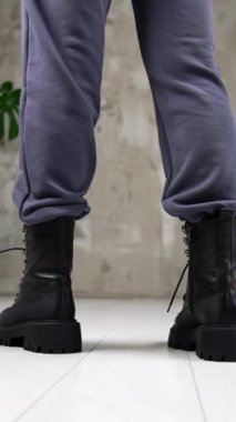Siyah traktör botlarıyla kameraya bakan kadın model. Stüdyoda modern şık ayakkabıları sergileyen bir kadın. Dikey video