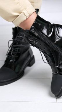 Plastik burunlu siyah çizme giyen bir kadın var. Model, rahat ve şık ayakkabılarıyla ayakta duruyor ve etrafında dönüyor. Kapatın. Dikey video