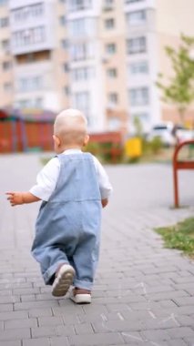 Geniş kotlu yakışıklı erkek bebek dışarıda yürüyor. Yazın yürüyüş yapan sevimli bir çocuk. Dikey video.
