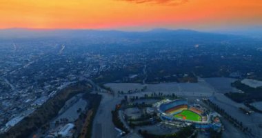 Dodger Stadyumu, Los Angeles, Kaliforniya, ABD. Stadyumun etrafındaki yoğun şehir manzarası. Arkaplanda, dağ sırasının üstündeki turuncu gökyüzü. Üst görünüm.