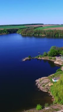 Rıhtımda arabaları olan otomobil yolu. Güneşli bir günde gök mavisi nehri üzerinde uçan bir dron. Tarımsal alanlar arka planda. Dikey video