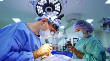 Cerrahi hoparlörlü erkek doktor metal bir alet alır ve ona dokunur. Beyin cerrahı ameliyatta çeşitli aletler kullanır. Düşük açı görünümü.