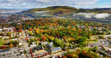 Dağların yakınlarındaki pitoresk şehirde renkli ağaçlar. Dağın eteğindeki nehrin üzerinde açık beyaz bulutlar asılı. Vermont, New England, ABD. Üst görünüm.