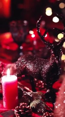 Noel 'de bir şenlik masasında parlak geyik oyuncağı süslemesi. Noel kutlaması için mumlar ve gözlüklerle süslenmiş güzel bir masa. Şenlik havası. Dikey video