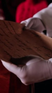 Mektubu tutan beyaz eldivenli Noel Baba 'nın elleri. Noel Baba mektubu masanın üzerine Noel kartlarının arasına koyar. Dikey video