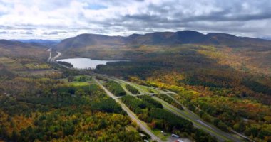 Yoğun ormanlarla kaplı engin doğa manzarasını otoyollar geçer. Dağların eteğinde küçük bir göl var. Panoramanın üstündeki bulutlu gökyüzü.
