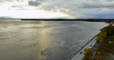 Sıkıcı gündüz vakti engin su manzarası bulutlu gökyüzünü yansıtıyor. Rıhtımdaki otoyolda çok az araba hareket ediyor. Hava görünümü.
