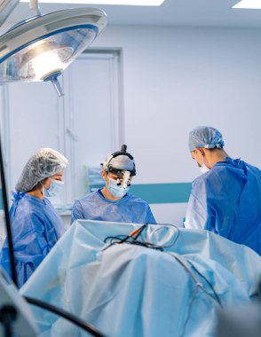Modern hastanedeki cerrahi ekibi. Bir cerrahi ekibi, tam donanımlı bir hastane ameliyathanesinde hastalarına özen ve özen göstererek iş birliği yapıyor..