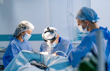 Ameliyathanede çalışan cerrahlar. Ameliyat önlüğü ve maskeli bir cerrah ekibi açık ve steril bir hastane ortamında hassas bir ameliyat gerçekleştiriyor..