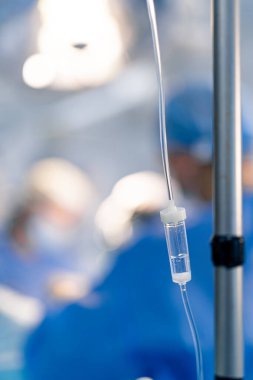 Serum takılı cerrahlar görüş alanında. Bir tıbbi ekip, ön planda belirgin bir şekilde damardan damlayan bir cerrahi müdahaleye tabi tutuluyor..