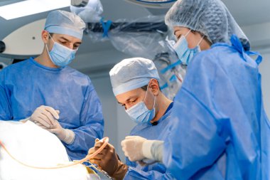 Hastanede ameliyat yapan bir cerrahi ekip. Cerrahi ekip bir ameliyathanede tibbi bir prosedür sirasinda bir hastaya odaklanarak gayretli bir sekilde calisiyor..