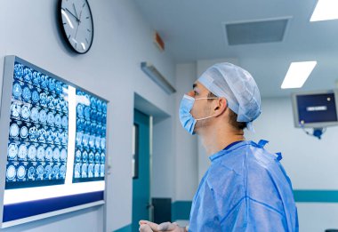 Doktor hastanede beyin taramalarını inceliyor. Bir sağlık çalışanı, koruyucu giysi ve maske takarken hastane ortamındaki monitörde beyin taraması yapar..