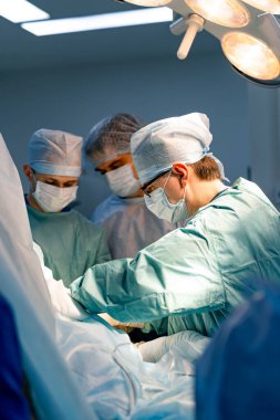 Ameliyathanede çalışan cerrahlar. Cerrahlardan oluşan bir ekip steril bir ortamda hastalarına dikkatle odaklanarak bir operasyon gerçekleştiriyor..