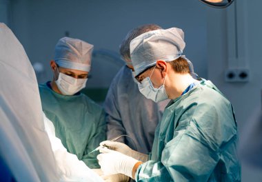 Hassas bir hastane operasyonunda cerrahlar. Tıp uzmanları, iyi donanımlı bir ameliyathanede hassas aletler kullanarak karmaşık bir cerrahi prosedüre odaklanırlar..