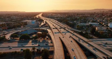 Batan güneş, Los Angeles, Kaliforniya, ABD 'de çok şeritli kavşak yollarını aydınlatıyor. Yolların üstündeki İHA görüntülerinde sayısız araba var..