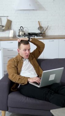 Genç adam evde bilgisayar oyunu oynuyor. Gergin adam mutfak arka planında dizüstü bilgisayarla kanepede yatıyor. Dikey video