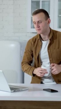 Freelancer dizüstü bilgisayarla konuşuyor. Genç adam mutfakta video görüşmesi sırasında biriyle konuşuyor. Uzaktan kumanda. Dikey video