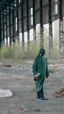 Radyoaktif bölge. Güvenlik üniformalı bir insan ve terk edilmiş duvarları ve çatısı olan terk edilmiş bir binada gaz maskesi. Kimyasal saldırı. Hava kirliliği. Dikey video