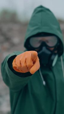 Kıyametler sonrası bölgede hayatta kalan biri. Yeşil takım elbiseli, gaz maskeli ve güvenlik eldivenli bir adam yıkılmış bir yerde duruyor ve parmağını kameraya doğrultuyor. Dikey video