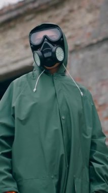 Güvenlik giysisi ve solunum cihazıyla tanınmayan biri. İnsan giysisi giyip yıkılmış binanın arka planında birini arıyor. Kimyasal saldırı. Dikey video