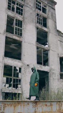 Radyoaktif bölgede biri var. Yıkılan binaların arka planında yürüyen kimyasal koruyucu giysili ve maskeli bir insan. Biyolojik saldırı. Dikey video