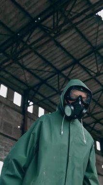 Koruyucu üniformalı ve gaz maskeli biri. Kimyasal saldırı sonrası kirlenmiş bölge. Yıkılan binanın arka planında tehlikeli madde kıyafeti giyen kadın. Dikey video