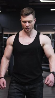 Formda bir adamın portresi. Spor yaptıktan sonra modern spor salonunda yürüyen kaslı bir vücut geliştirici. Spor merkezinde siyah cüppeli yakışıklı bir sporcu. Dikey video