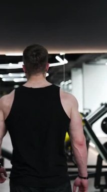 Sportmendeki acımasız adam. Modern fitness merkezinde kaslı vücutlu yakışıklı bir sporcu. Sportif yaşam tarzı. Dikey video