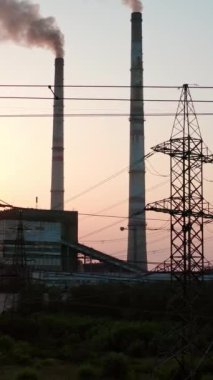 Gün batımında zararlı enerji santralinin panoramik görüntüsü. Akşamları gökyüzünde duman yığınları olan büyük fabrikanın yanındaki elektrik direkleri. Kamera yükseliyor. Dikey video