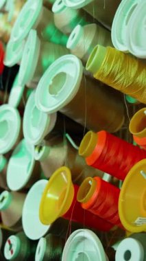 Masanın üzerinde farklı renkte iplik makaraları var. Dikiş endüstrisi için renkli iplik koleksiyonu. Pamuk iplikli birçok makaranın arka planı. Dikey video