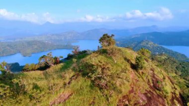 Dağların tepesinde otlar ve ağaçlarla kaplanmış bir şekilde uçmak. Gök mavisi su manzaraları, arka planda resimsel kayalarla çevrili. Hava görünümü.