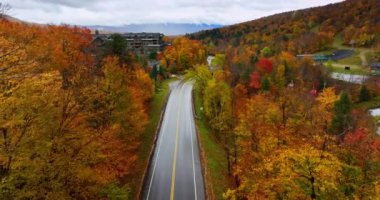 Kablolu yolda birkaç kulübe hareket ediyor. Sonbaharda güzel renkli ormanları geçen otobanın üzerindeki İHA görüntüleri..